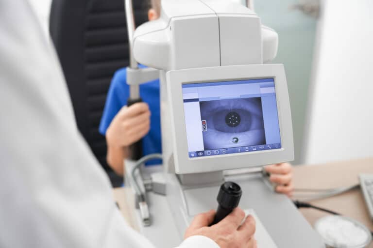 Little girl looking at equipment and doctor testing eye pupil in optical store. Concept of eye care and health.