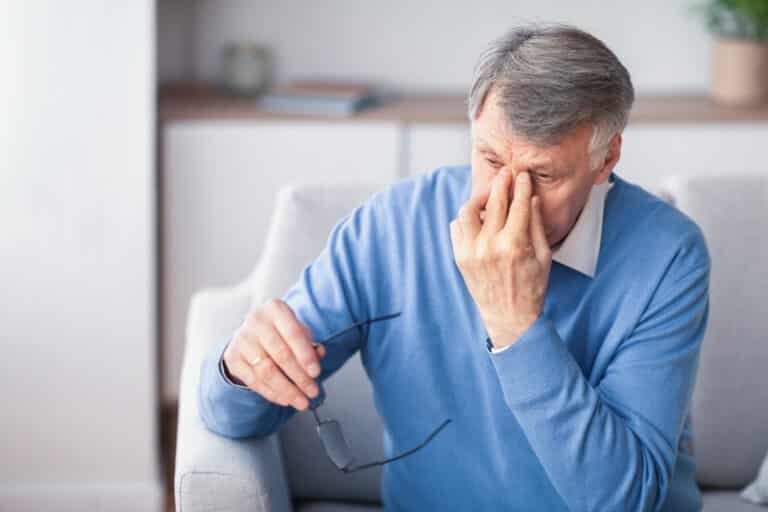 elderly man massaging nose bridge sitting on couch