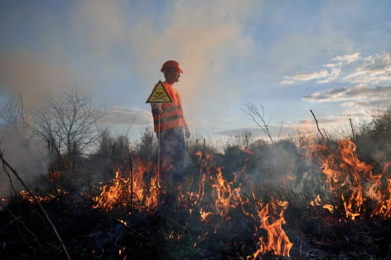 Fireman ecologist fighting fire in field in evening