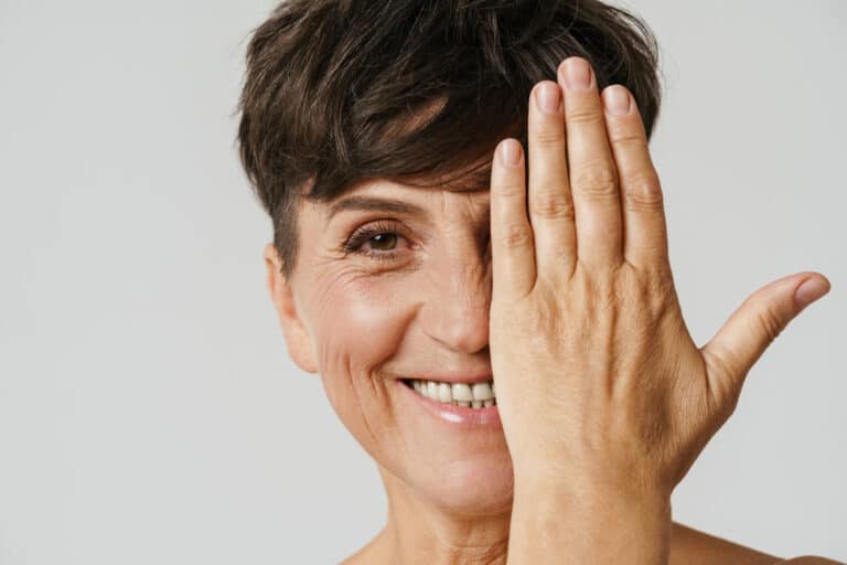 Mature half-naked woman smiling while covering her eye isolated over white background