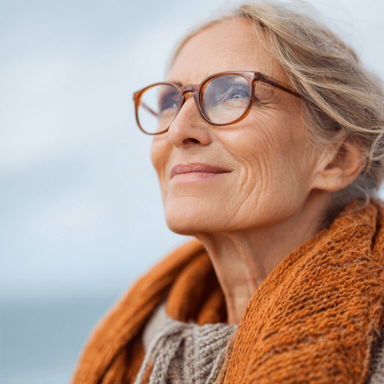 Elderly woman smiling with glasses outdoors.